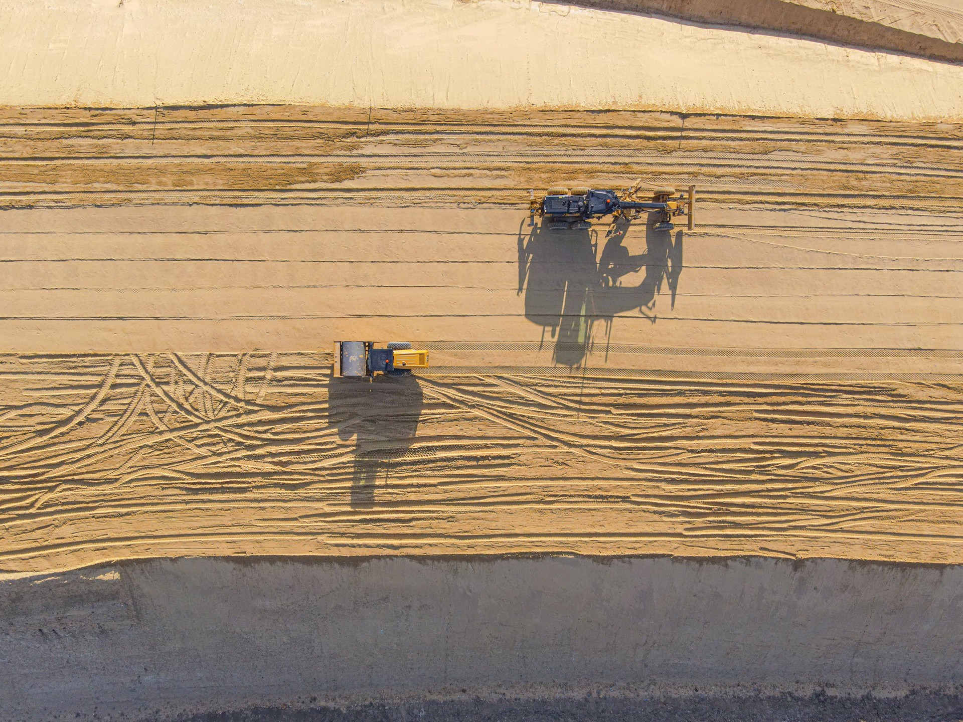 Construction roller and grader on sand, aerial view