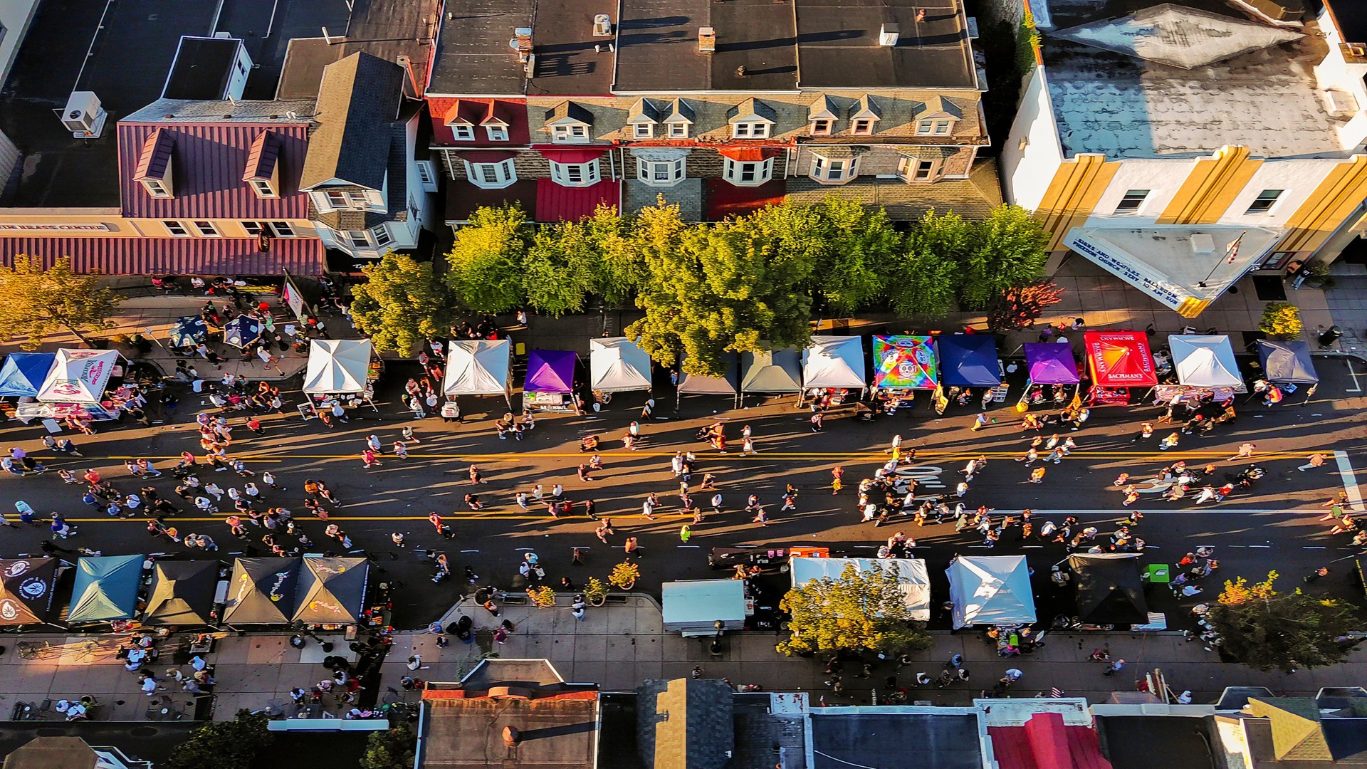 Small town party in Fall: autumnal Street Food Festival with busy food trucks lining lively street. Aerial top view